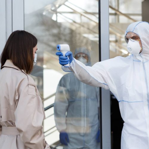 Man in coronavirus hazmat measuring temperature of a woman